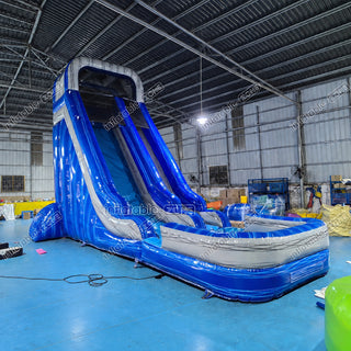 A large inflatable blue and gray slide parkour course inside a warehouse, with a water pool at the base and visible 'inflatable-world' watermarks across the photo.